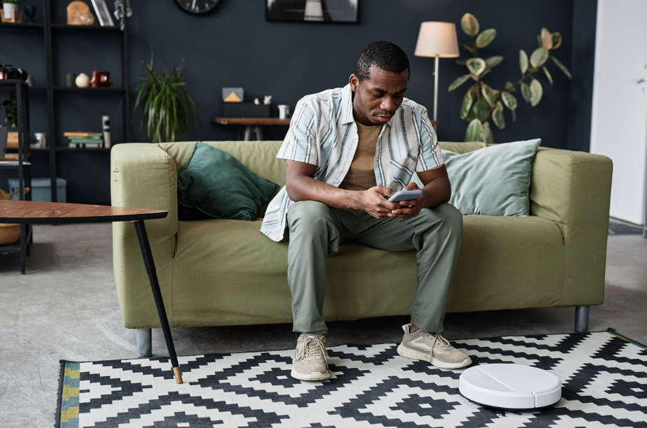 White robot vacuum moving off a black and white patterned rug while a man sits on a green sofa