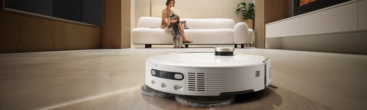 MOVA V50 robot vacuum with twin mop pads cleaning a dark living room floor while a woman sits on the sofa